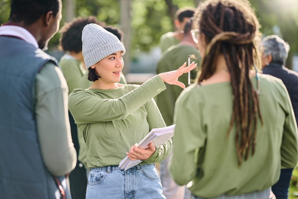 Volunteer schedule, community cleaning leader and charity service outdoor with Asian woman talking.